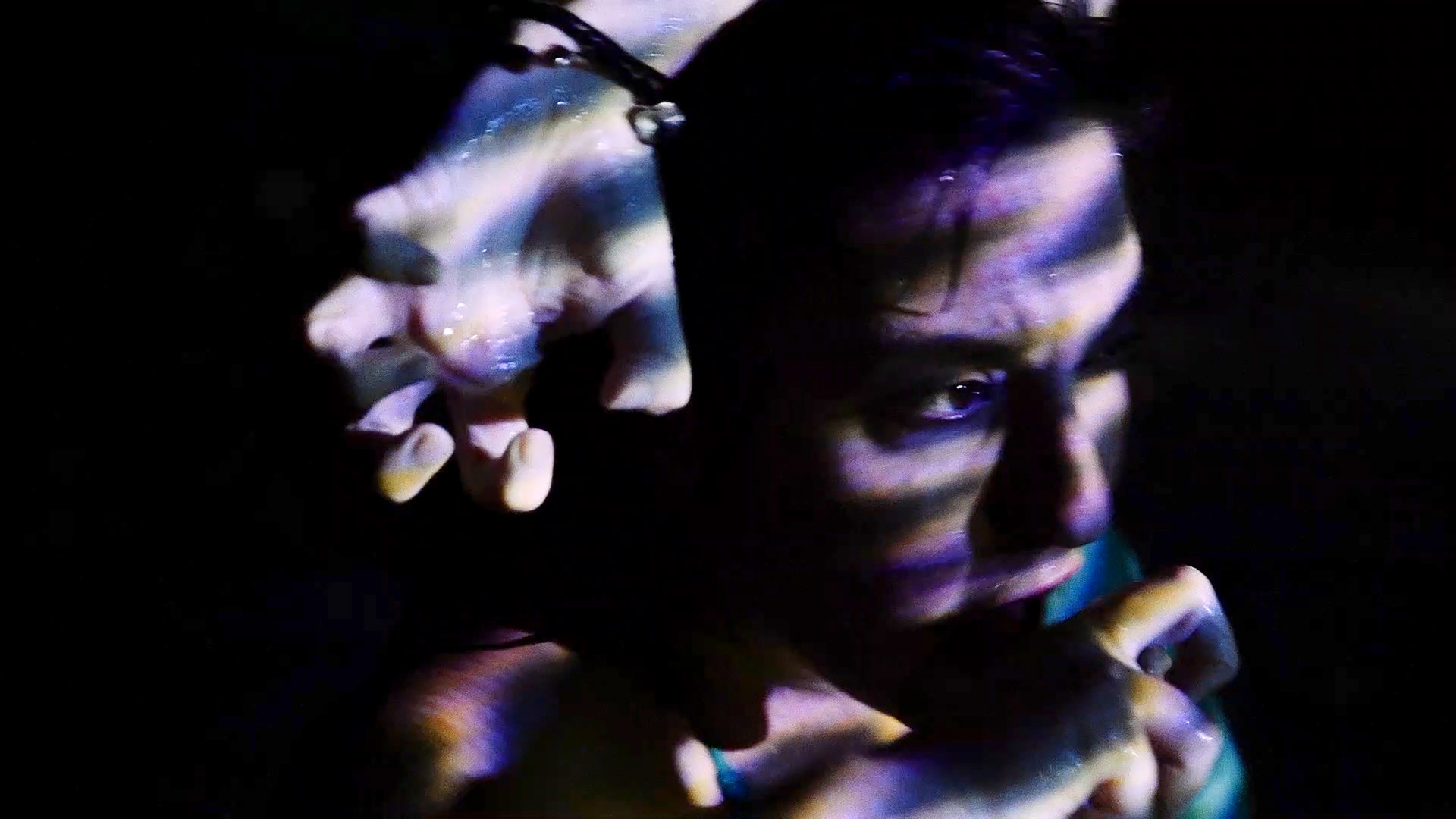 Still from CoNscience: Close-up of a person's face and shoulder in darkness, illuminated by streaks of purple, blue, and white light. A translucent hand with similar light patterns appears behind them.